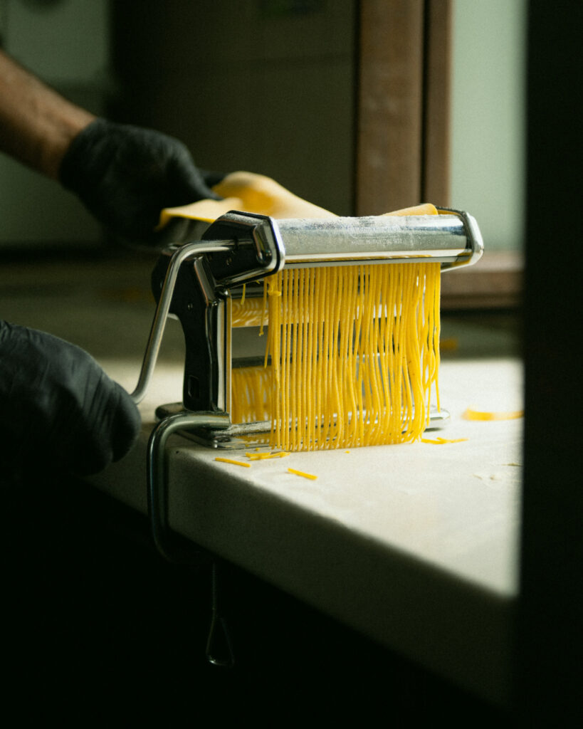 Primo piano di due mani con guanti che azionano una macchina manuale per la pasta fresca