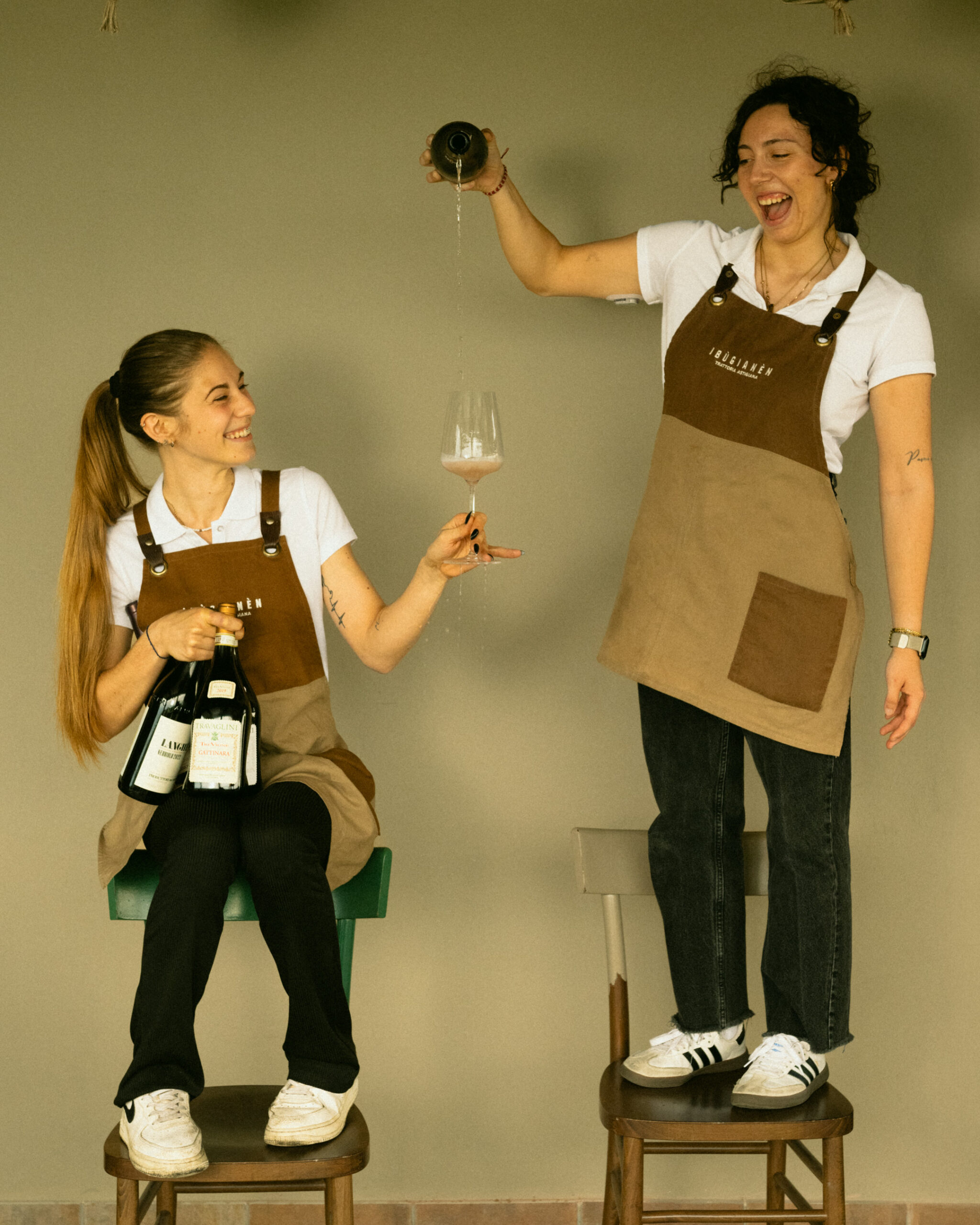 Due giovani cameriere con il grembiule del ristorante versano una bottiglia di vino