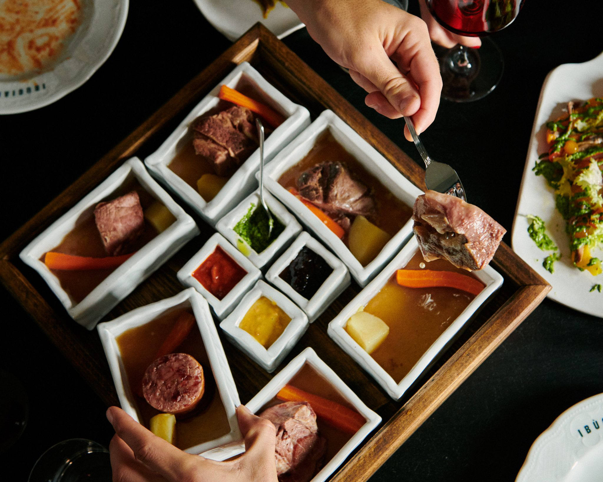 Visione d'insieme di ciotole quadrate con all'interno i pezzi del bollito misto piemontese e i sughi per accompagnarlo