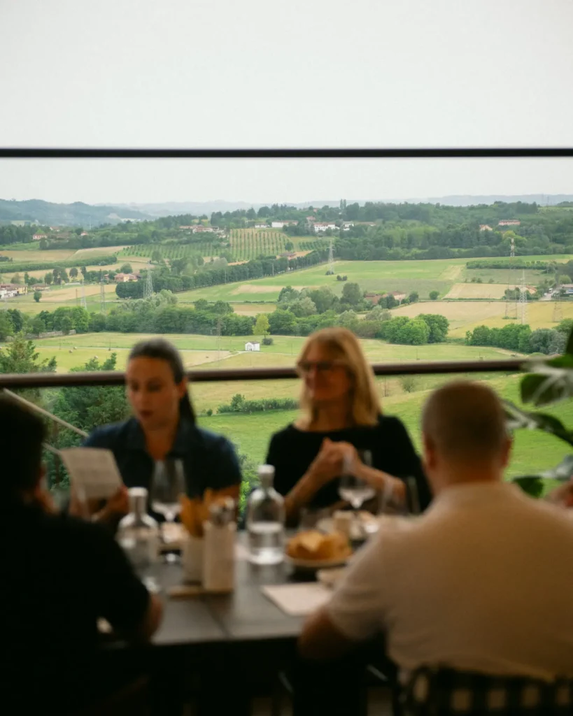 Persone sedute a un tavolo di ristorante, alle spalle il panorama delle colline del Piemonte