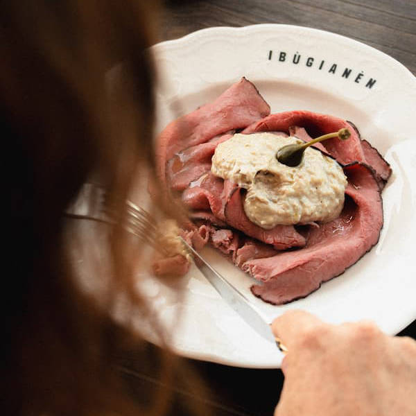 Una persona di spalle intenta a tagliare il il vitello tonnato nel suo piatto