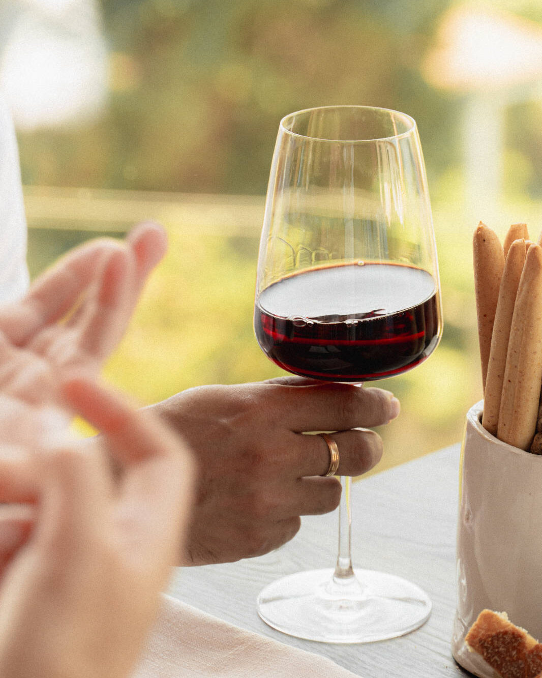 Primo piano di una mano che regge un bicchiere pieno per metà di vino rosso