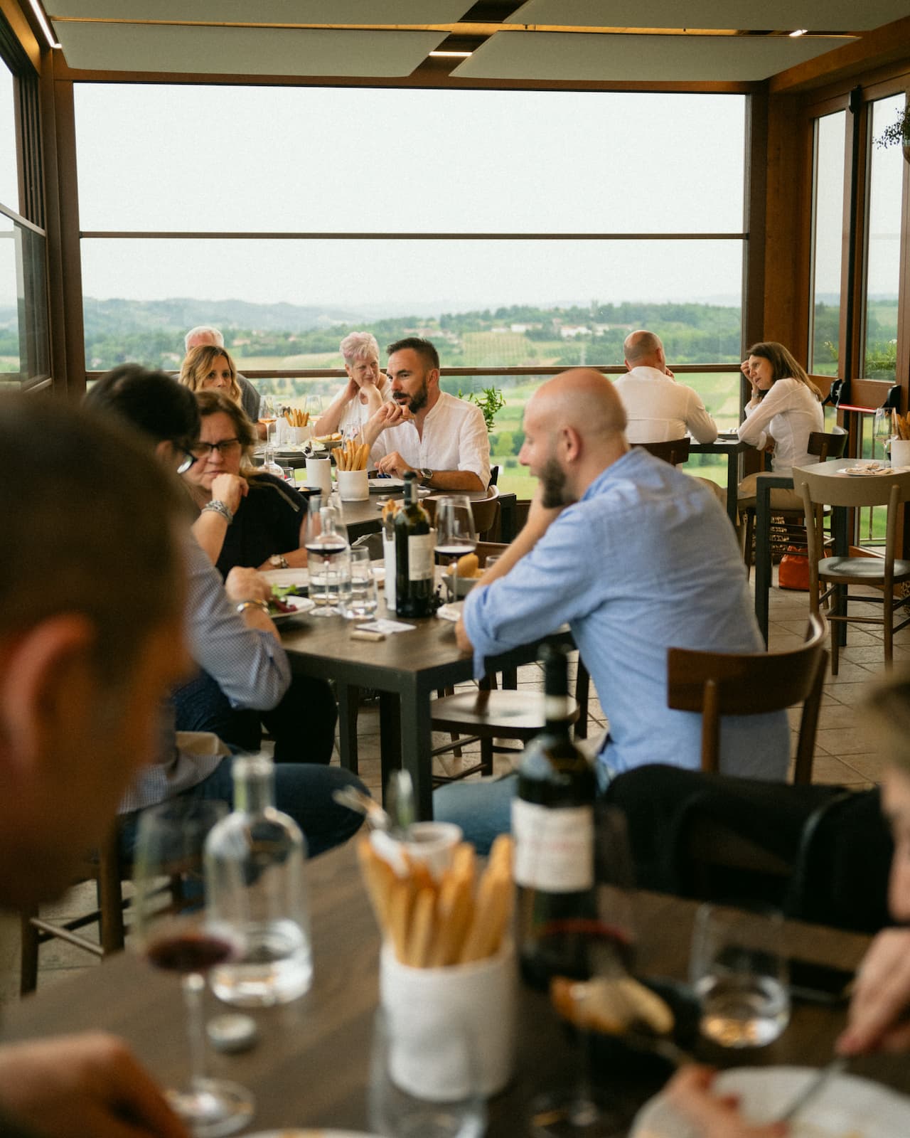 Persone ai tavoli di una sala di un ristorante con vista sulle colline del Piemonte